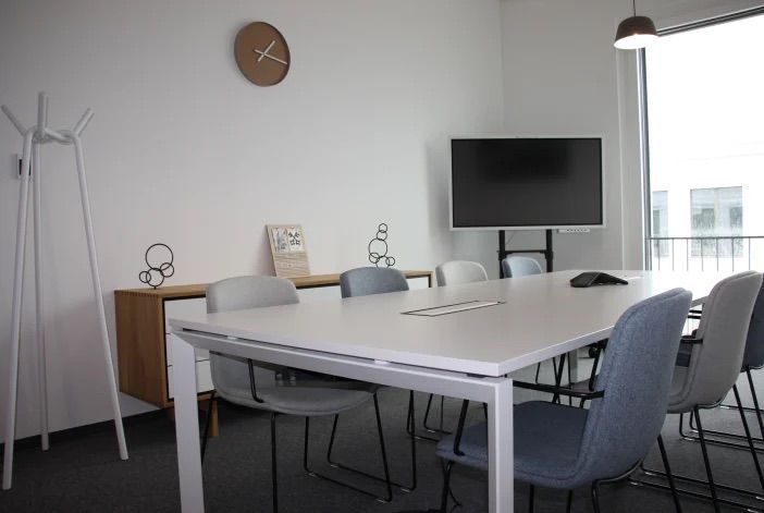 Besprechungsraum mit großem Konferenztisch, Bildschirm und hellen Fensterflächen